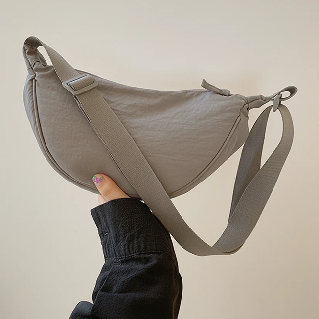 Half moon crossbody sling bag in grey held up to show the adjustable strap