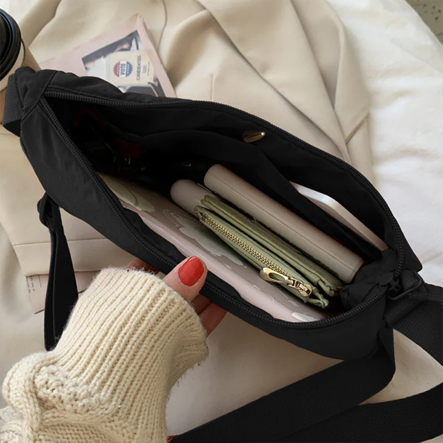 Half moon crossbody sling bag in black opened to show the inside compartment with wallet and phone