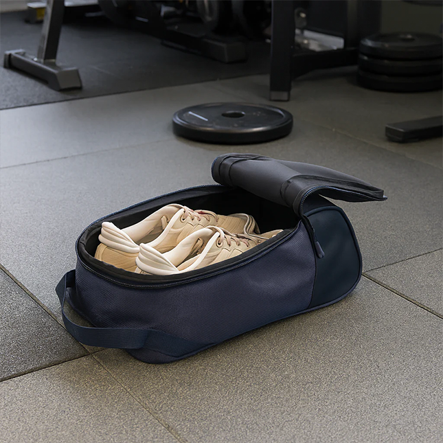 Solaris atlas shoe bag in navy opened on a gym floor with sneakers inside