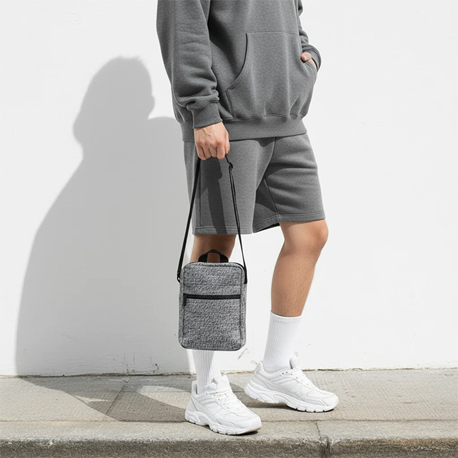 Kairos sling bag in grey carried by the top handle